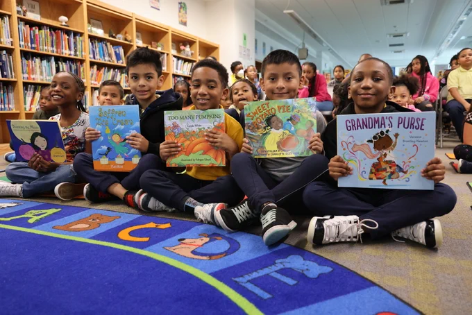 Several students hold up books to show their covers.