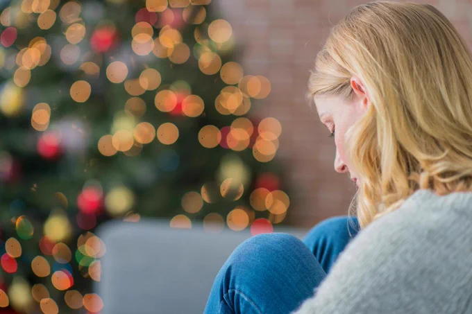 A person sitting by a Christmas tree with blurred lights in the background.