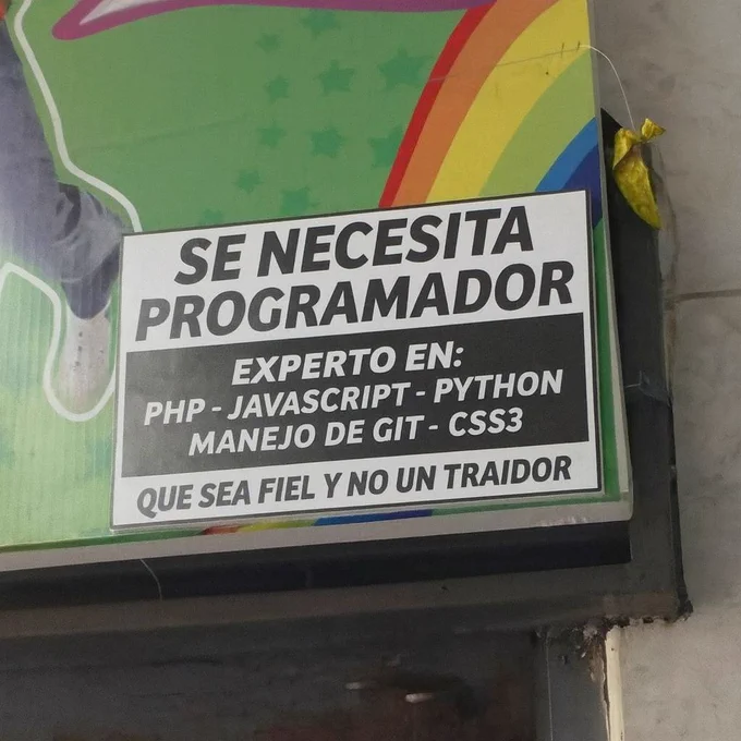 Cartel colgado en una pared que dice “Se necesita programador experto en PHP, JavaScript, Python, manejo de Git y CSS3” y remata con “que sea fiel y no un traidor”, como si Git hubiera dejado traumas personales en la empresa.