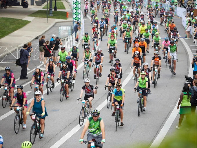 Pelotonia riders showing the power of community to support cancer research in the Pelotonia Ride Weekend fundraising event. The image shows a street full of people riding bikes in the direction of the camera, with onlookers viewing from either side of the street.