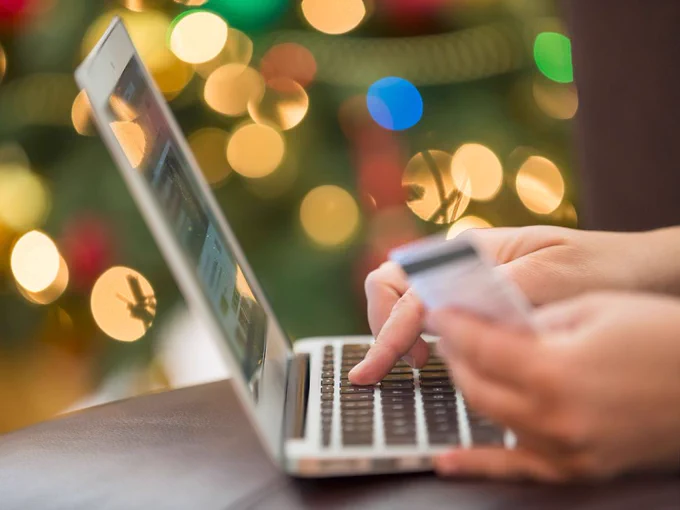 someone using a lap top surrounded by holiday lights while holding credit cards in hand