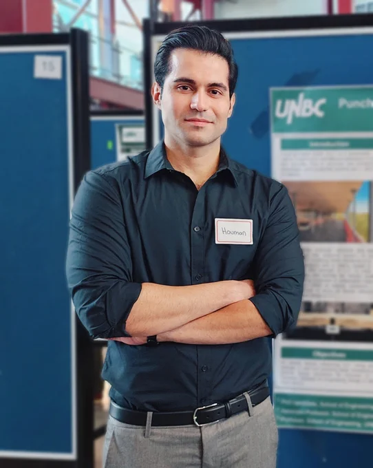Person standing with arms crossed in front of a UNBC promotional display.