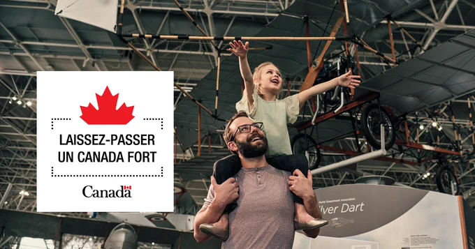 Un enfant aux longs cheveux blonds est assis sur les épaules de son père au Musée de l'aviation et de l'espace du Canada. Tous deux sourient et regardent un avion. Le badge laissez-passer un Canada Fort se trouve dans le coin gauche de l'image.