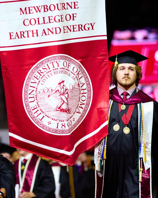 Graduate holding the University of Oklahoma, Mewbourne College of Earth and Energy banner at a graduation ceremony.