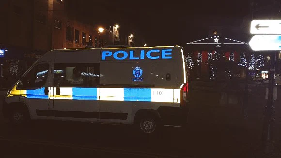Image of a police van in front of church. It is night time but the outline of the church is illuminated by christmas lights