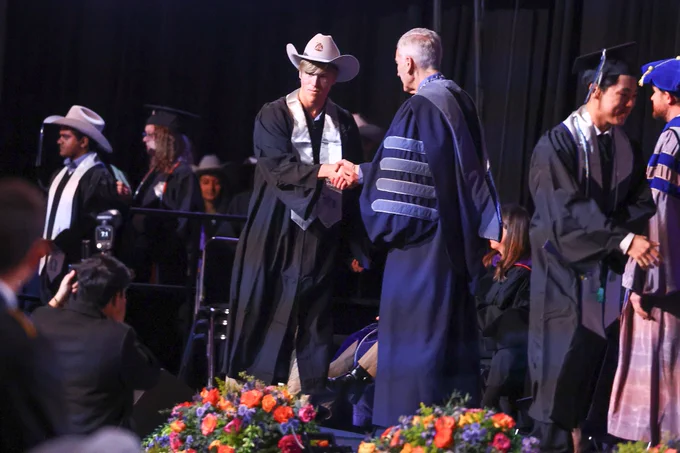 Former Mines Soccer player Tommy Jernigan shakes hands with Mines President Paul Johnson at graduation as he earns his degree in Computer Science 