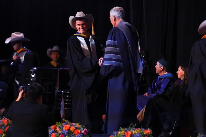 Former Mines Soccer player Caelin David shakes hands with Mines President Paul Johnson at graduation as he earns his Master's degree in Quantitative Biosciences and Engineering 