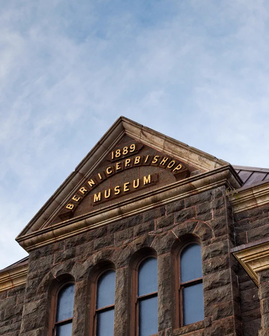 Facade of the Bernice Pauahi Bishop Museum, established 1889, featuring arched windows and stone masonry against a blue sky.