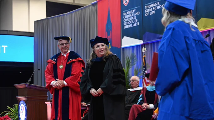 Dean Blair and President Gormley greet a graduate on stage before she received her diploma.