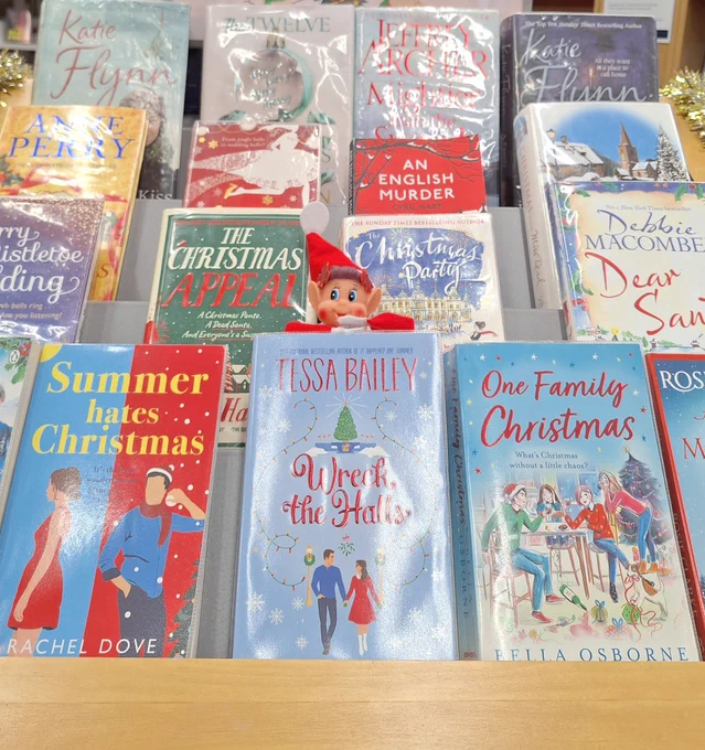 A selection of Christmas fiction books on display with a elf figure half way down.