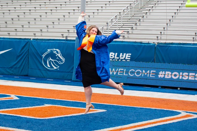 Graduate celebrating on Boise State University's blue football field.