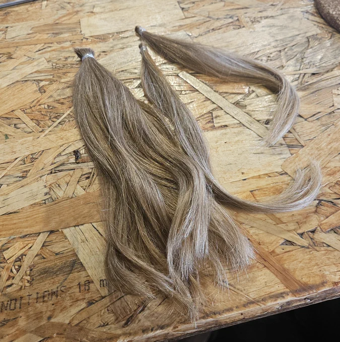 Three ponytails of hair cut off, laying on a wooden surface