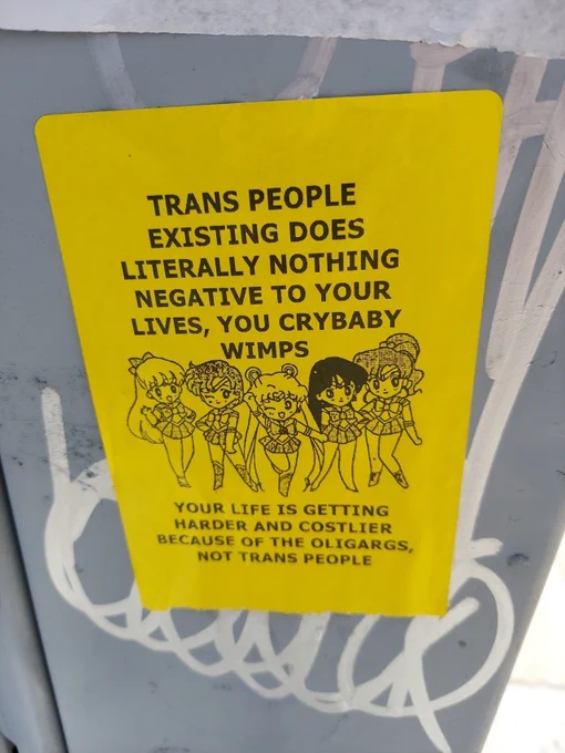 Sailor Scouts on a sign that reads "Trans people existing does literally nothing negative to your lives, you crybaby wimps. Your life is getting harder and costlier because of the oligarchs, not trans people. 