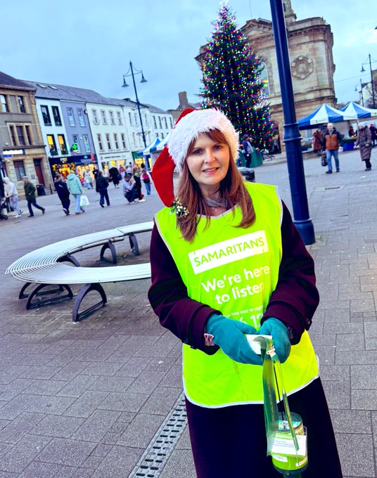 Image of Caoimhe Archibald in front of Coleraine Town Hall and Christmas tree wearing a Samaritans hi-viz vest and Santa hat 🎅🏽🎄