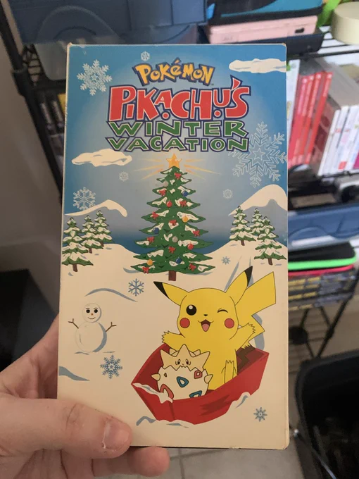 A VHS tape with a cover that’s titled “Pikachu’s Winter Vacation.”  Cover also shows Pikachu and Togepi in a sled with a snowy background and a Christmas tree