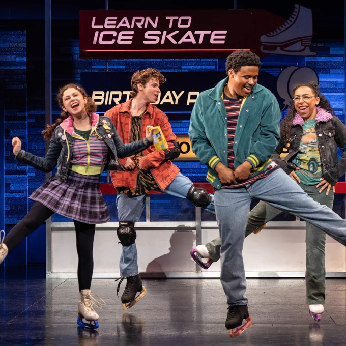 Four individuals joyfully dancing on stage with ice skates on, in front of a backdrop that reads "Learn to Ice Skate."