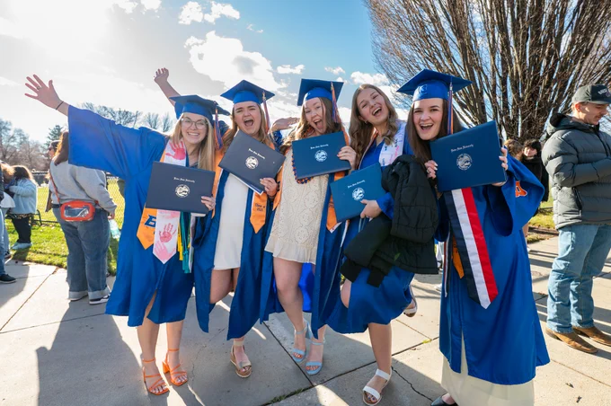 A group of Boise State graduates smiling and posing with their diplomas. 
