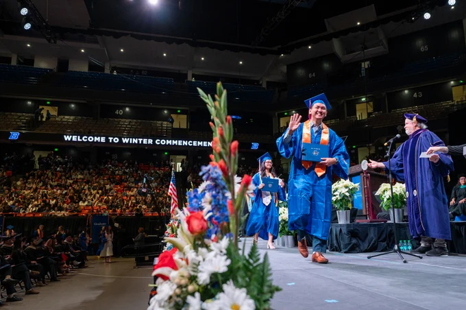 Boise State graduate smiling and walking across a stage and receiving their diploma. 
