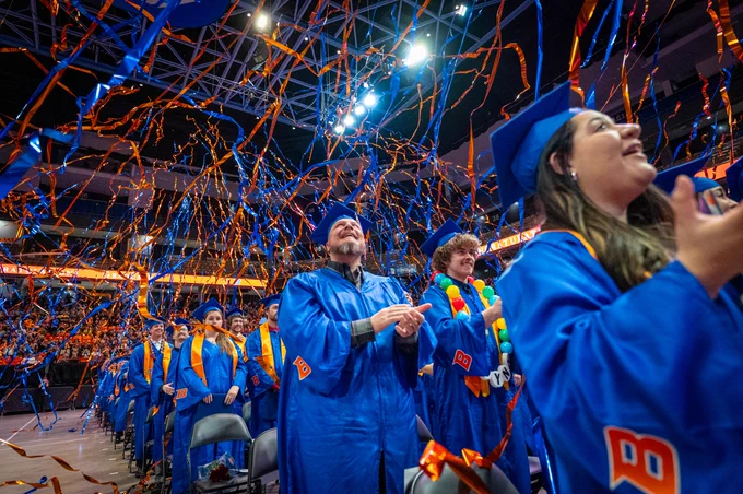 Boise State graduates clapping and watching blue and orange streamers fall in celebration during commencement.
