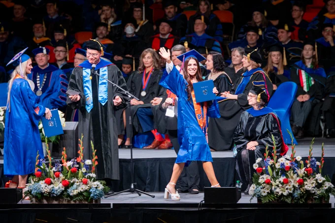 Boise State graduate smiling and walking across stage after receiving their diploma. 
