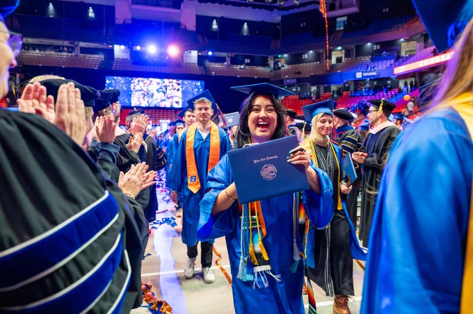 Boise State graduate smiling and showing off their diploma at commencement. 
