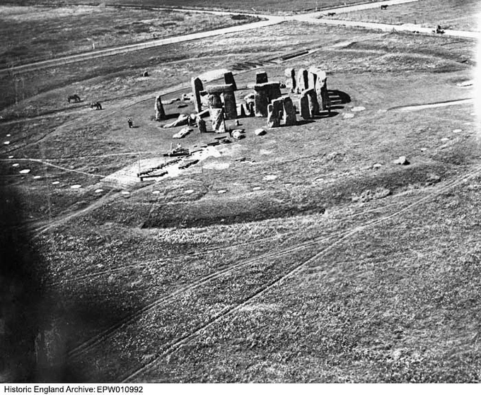 A black-and-white oblique aerial photograph showing some standing stones in a grassy field. 