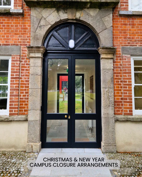Entrance to a brick building with a black door and a sign above it reading 'Christmas & New Year Campus Closure Arrangements', visible below the door.