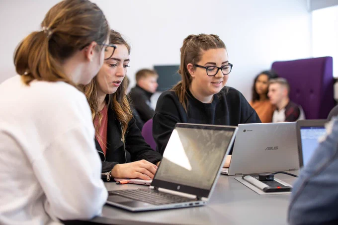 Group of students working together at a table using laptops in NESCol city campus.