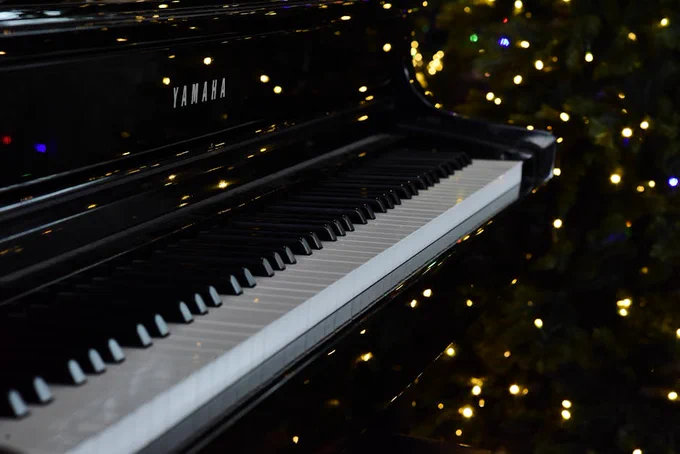 A close-up of a black grand piano keyboard with festive Christmas lights in the background.