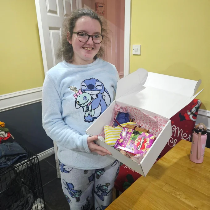 Girl in pyjamas holding an open gift box with snacks and colourful items inside.