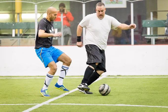 Three men battle for a soccer ball during an indoor soccer game.