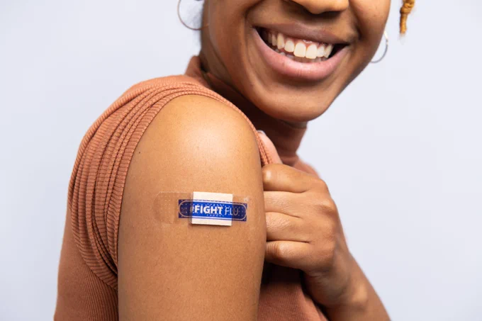 A woman wears a blue bandage on her upper arm after receiving a flu vaccine. #FightFlu and CDC branded logos are in the bottom right corner of the image. 