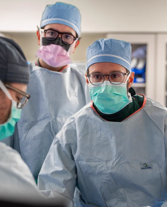 Three medical professionals in surgical attire, including masks and caps, standing in an operating room.