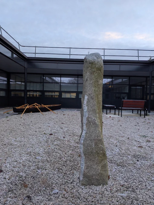 Ogham stone inscribed with 'Ollscoil Mhá Nuad' in ogham script (foreground) with traditional currach (background) in Garraí na Gaeilge in the Arts Building, Maynooth University