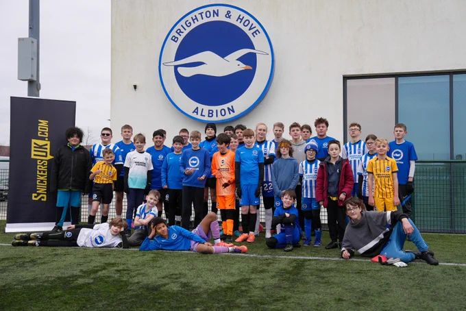 A group photo of the participants who attended our disability camp. There's a SnickersUK banner to their right, a Brighton badge above them, and plenty of Albion tops on show!