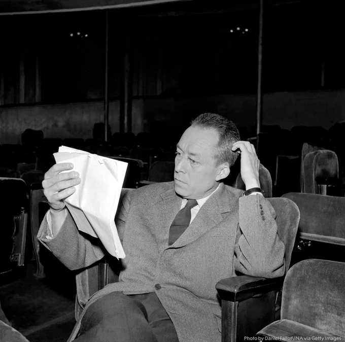 Albert Camus sitting in a theatre reading a document.