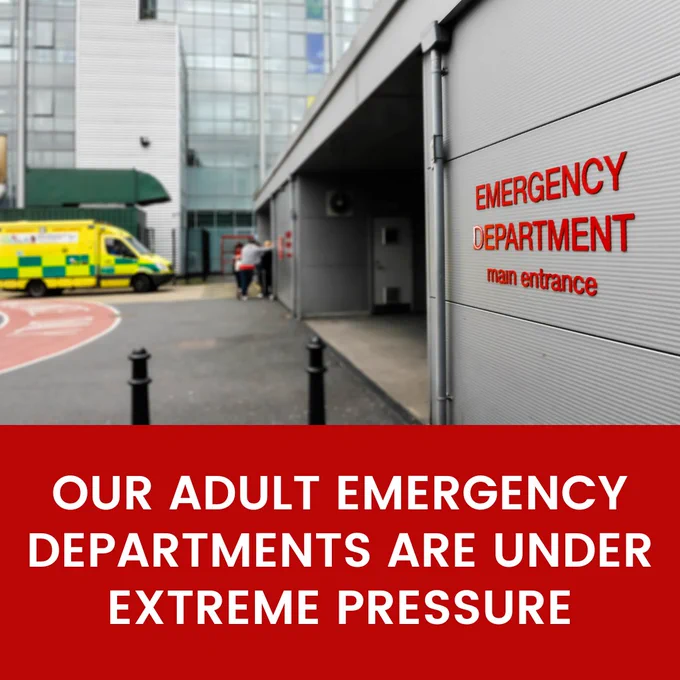 An ambulance waiting at an Emergency Department. Text on a red banner at the bottom reads: Our Adult Emergency Departments are under extreme pressure.