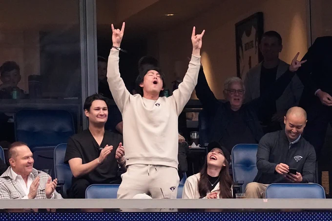 Tatsuya Imai stands making an H with his hands at the Houston Texans game. He wears a cream-colored sweatshirt and sweatpants.