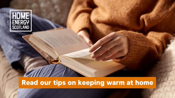 A person is sitting with their legs crossed on a couch. They are wearing a warm autumnal woolen jumper and woolen socks. They are turning the page of a book they are reading. The overlay on the image reads ' Read our tips on keeping warm at home' 