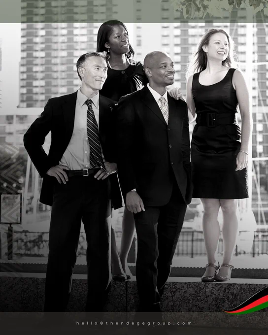 Monochrome photograph: four professional colleagues (diverse ethnicities) in business attire on urban rooftop, office buildings background, unified forward-gazing posture. Pan-African flag colours bottom right, hello@thendegegroup.com at bottom. Development finance demands multidisciplinary expertise: legal specialists structuring REITs, agricultural economists designing smallholder programmes, infrastructure engineers planning utilities, cultural preservation experts. The Ndege Foundation© implements pan-African, pro-African development guided by The African Charter: transparency, community benefit, environmental stewardship, cultural respect. Institutional capacity multiplies through coordinated specialisation. African Charter: www.thendegegroup.com/the-african-charter. Collaboration compounds outcomes. Development Finance | Multidisciplinary Teams | Pan-African Development | The Ndege Foundation© | The Ndege Group®, Africa’s Sovereign Development Trust® (ASDT)