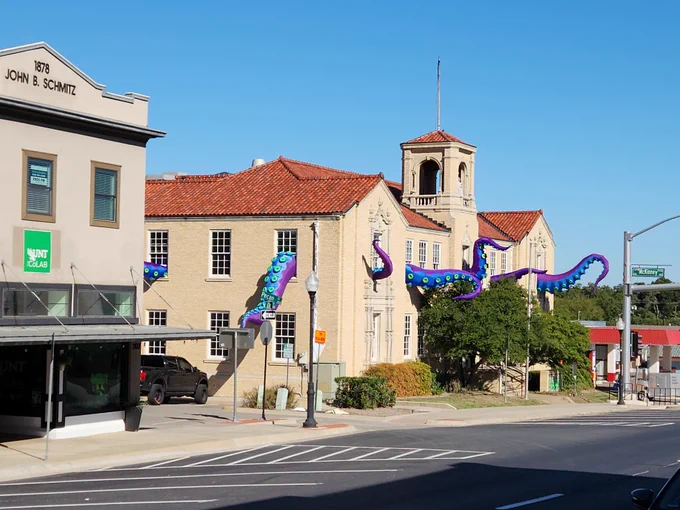 A photo of a two-story building with multiple blue and purple octopus tentacles coming from windows.