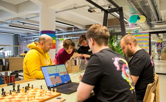 Een groep mannen en vrouwen in een kantoor aan een tafel waarop een schaakbord en een laptop staan.