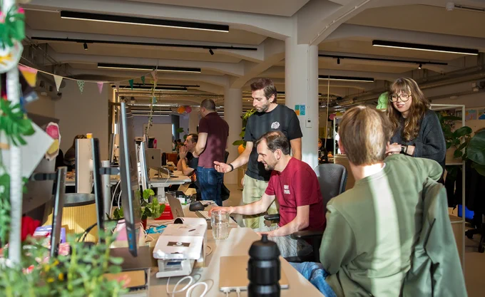 Een kantoorsetting met een groep mensen rond bureaus waarop schermen en laptops staan.