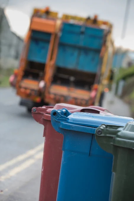 Red, blue and green bins facing a refuse wagon.