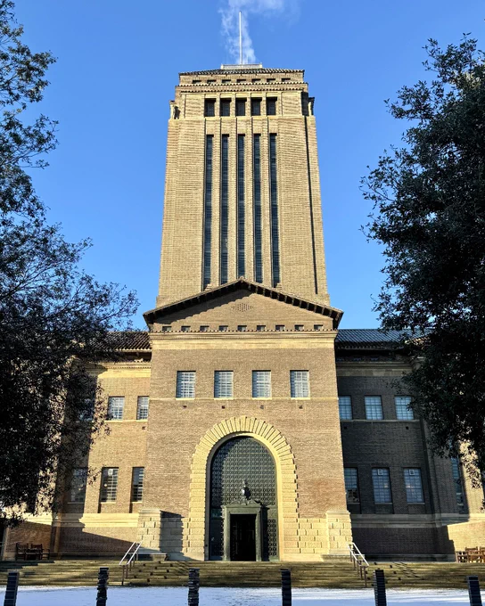 Cambridge University Library on a snowy day. We see the front of the building, including the tower. Snow lays on the ground and we see a plume of white steam coming out of the top of the tower.