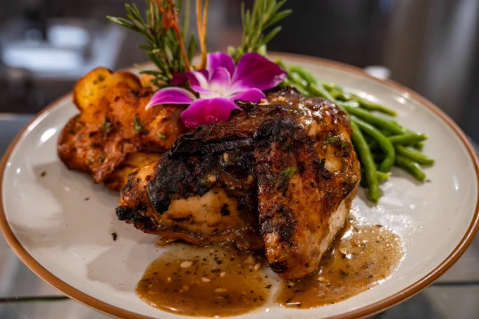 Spicy Roasted chicken with roasted potatoes, green beans decorated with a flower on a clay plate. 