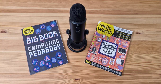 Two Hello World magazines on computing pedagogy and integrated computer science sit bedside a black podcast microphone on a wooden table.