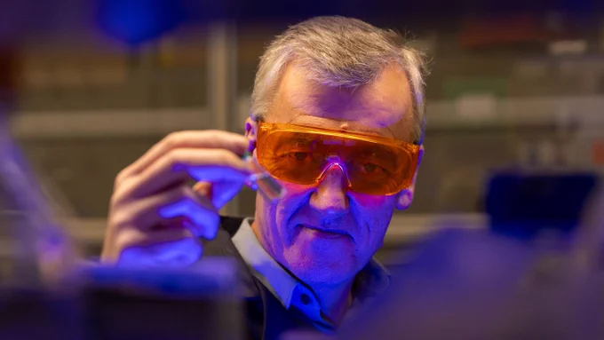 Full-color photo of David MacMillan in the lab at Frick, wearing goggles, with blue light shining on his face. Photo: Denise Applewhite