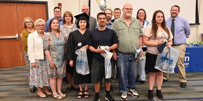 Aspire graduates, including one in a graduation cap and gown, stand at graduation while surrounded by faculty and staff from Marion Tech.