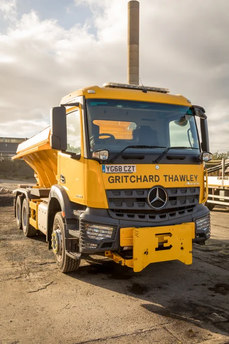 View of the front of a yellow gritter which has the name Gritchard Thawley